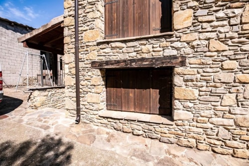 Exterior de apartamento de piedra en Montgat Pirineo con puertas de madera rústica y vistas a la montaña