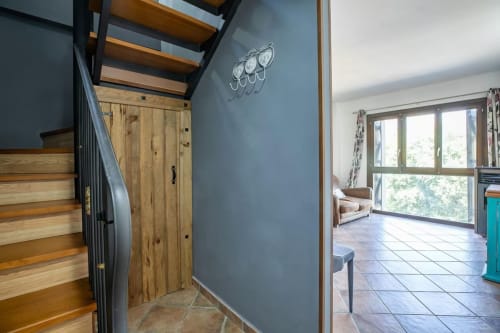 Entrada moderna de apartamento con escaleras de madera, pared azul grisáceo y sala de estar abierta con vistas a las montañas en Montgat, España