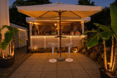 Terrazza bar esterna di Gan Eden B&B al tramonto con ombrellone arancione, sgabelli bianchi e piante tropicali a San Benedetto del