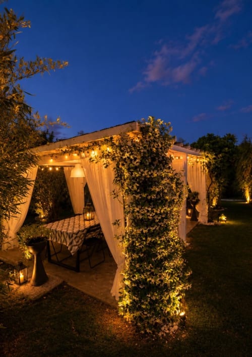 Pergolato illuminato al Gan Eden B&B con edera rampicante, tende bianche e zona pranzo al crepuscolo