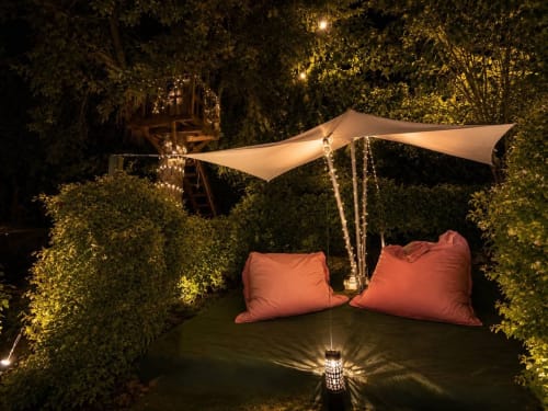 Lounge esterno illuminato a Gan Eden B&B con cuscini corallo, vela tenda e vegetazione rigogliosa a San Benedetto del