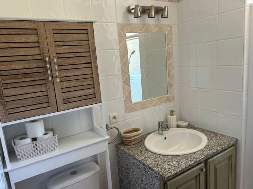 Salle de bain moderne de l'hôtel Vista D'oro avec plan de travail en granit, lavabo rond, meuble de rangement en bois et miroir encadré