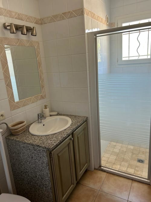 Salle de bain moderne de Vista D'oro avec vanité en granit, lavabo blanc, bordure de carrelage décoratif, miroir et douche à l'italienne
