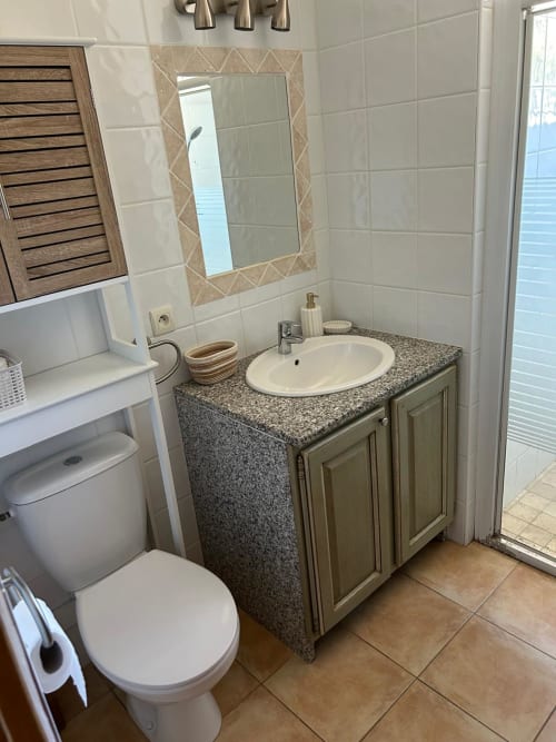 Salle de bain moderne à Vista D'oro avec lavabo blanc, plan de travail en granit, toilettes et miroir décoratif à Monacia d'Aullène