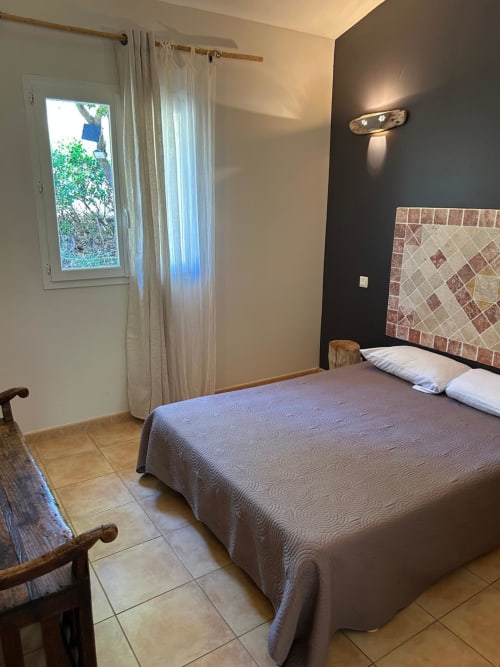 Chambre confortable à Vista D'oro à Monacia d'Aullène avec lit queen-size, mur d'accent sombre, tête de lit carrelée et vue sur le jardin
