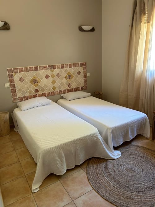 Deux lits jumeaux aux draps blancs et tête de lit en carrelage décoratif dans la chambre Vista D'oro, Monacia d'Aullène