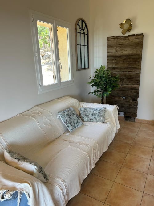 Salon lumineux à Vista D'oro, Monacia d'Aullène avec canapé crème, tête de lit en bois, plantes et portes-fenêtres donnant sur