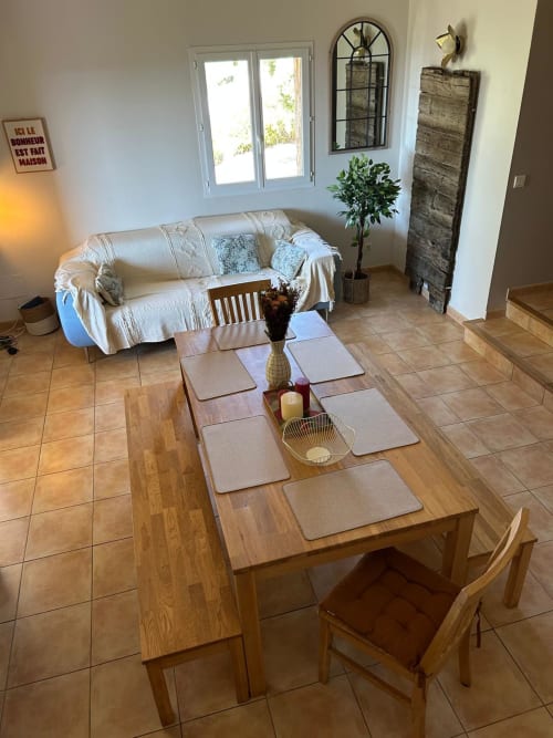 Salle à manger lumineuse à Vista D'oro avec table en bois, vue sur mer par portes vitrées, canapé crème et plantes