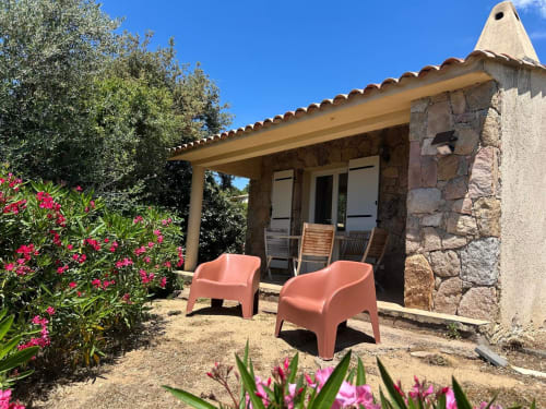Charmant cottage en pierre avec terrasse à Vista D'oro, Corse, agrémenté de chaises roses et de plantes fleuries
