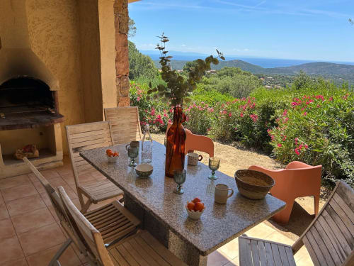Terrasse de restaurant en plein air Vista D'oro avec vue sur mer, table en pierre, chaises en bois, foyer et jardins méditerranéens