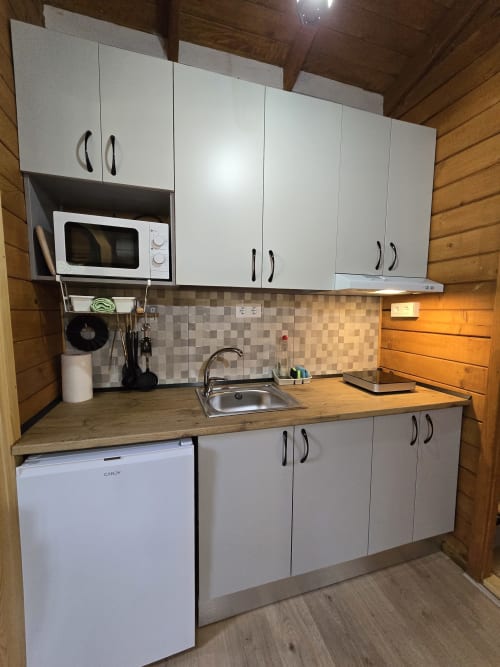 Moderna cocineta del Ecolodge de Cabañeros con gabinetes blancos, encimeras de madera, microondas, fregadero y refrigerador compacto