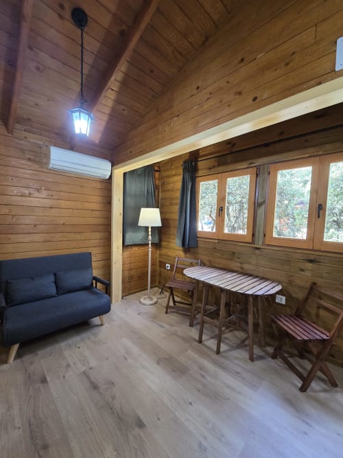 Acogedor interior de cabaña de madera en Ecolodge de Cabañeros con sofá azul, mesa de comedor y vistas al jardín