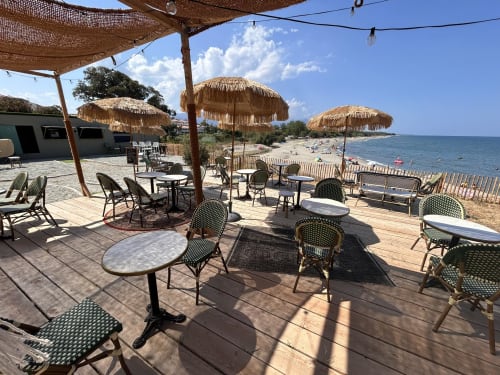Beachfront dining area at Résidence Marina di Bravone with thatched umbrellas, tables, and Mediterranean Sea views
