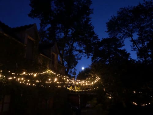 Cortile incantevole del Domaine de l'Ocrerie con luci scintillanti, luna piena e alberi alti a Pourrain