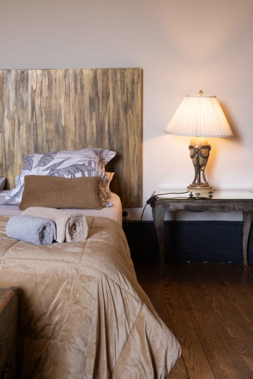 Chambre élégante à La vie de château B&B à Grignan avec tête de lit en bois, literie crème, lampe en laiton et parquet foncé.