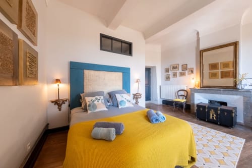 Chambre spacieuse à La vie de château B&B à Grignan avec tête de lit bleue, couvre-lit jaune, cheminée et vues sur les montagnes