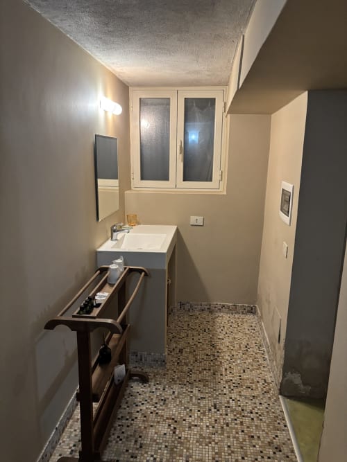 Modern bathroom in Casale Artemisia with sink, mosaic tile floor, and frosted window overlooking Capalbio garden