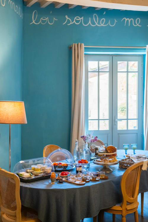 Élégante salle de petit-déjeuner à La vie de château B&B à Grignan avec murs turquoise, table ronde dressée avec pâtisseries et fruits frais