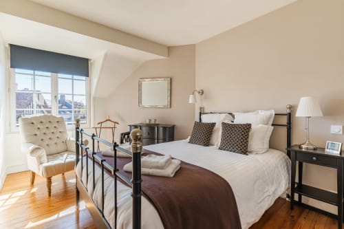 Elegant bedroom at Les Maisons de Pierre et Valérie B&B in Honfleur with wrought iron bed, cream armchair, and city views
