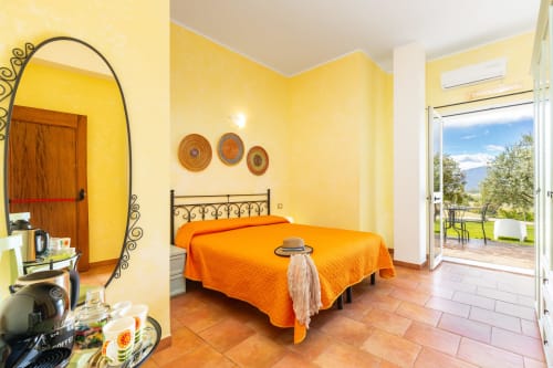 Bright yellow bedroom with orange bedspread, wrought iron bed frame, garden view at Agriturismo Chiai Francesco in Bari