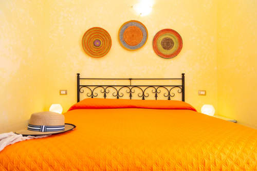 Bright yellow bedroom with orange bedding at Agriturismo Chiai Francesco in Bari Sardo, featuring decorative wall plates and