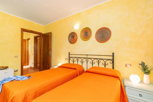 Bright yellow bedroom with twin orange beds, wrought iron headboard, and garden view at Agriturismo Chiai Francesco in Bari