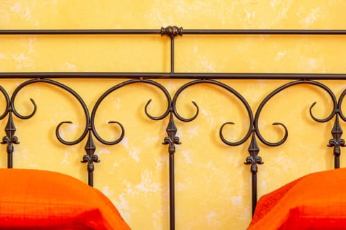 Ornate wrought iron headboard with scrollwork against yellow textured wall, orange bedding visible at Agriturismo Chiai