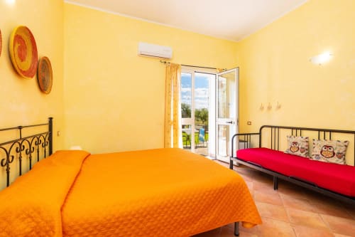Bright yellow bedroom with orange bed, red sofa, and garden views at Agriturismo Chiai Francesco in Bari Sardo, Italy