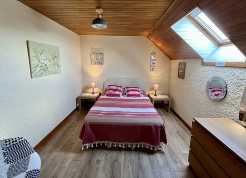Chambre douillette sous les toits au Gîte La Vieille Ferme de La Doinie avec literie rayée rouge, plafond en bois, lucarne et vue sur le jardin