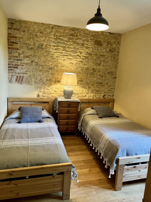 Chambre cosy avec deux lits jumeaux au Gîte La Vieille Ferme de La Doinie : murs en pierre, lits en bois et ambiance chaleureuse à Saint-Geniès