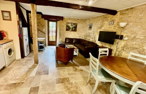 Séjour ouvert du Gîte La Vieille Ferme avec murs en pierre, sièges en cuir, table à manger et télévision à Saint-Geniès