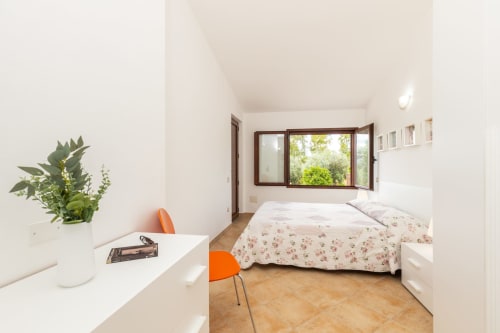Bright bedroom with floral bedding, wooden window with garden view, white desk, orange chair at Agriturismo Chiai Francesco