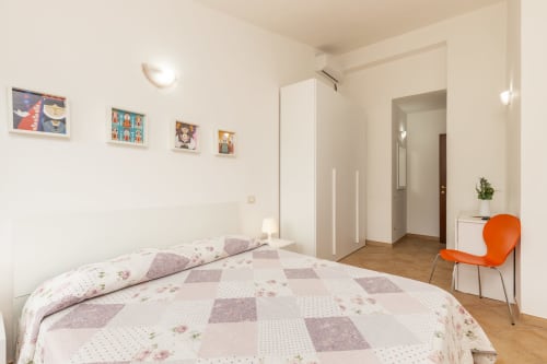 Bright bedroom in Agriturismo Chiai Francesco apartment with floral bedding, white wardrobe, orange chair, and colorful wall