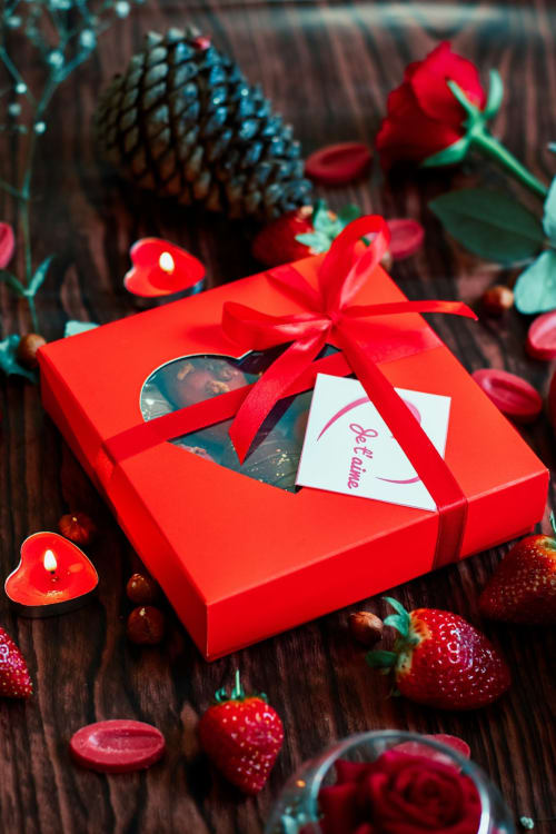 Boîte cadeau rouge avec ruban entourée de roses, fraises et bougies en forme de cœur au Mas Aurel de Provence