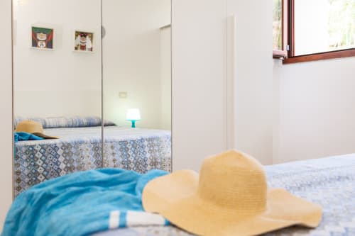 Sunny bedroom with mirrored wardrobe, straw hat and blue towel on bed at Agriturismo Chiai Francesco, Bari Sardo