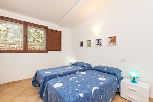 Cozy bedroom at Agriturismo Chiai Francesco in Bari Sardo with twin beds, starry blue bedding, wooden windows, and garden
