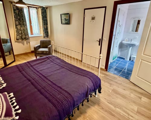 Chambre spacieuse à La Vieille Ferme de La Doinie avec literie violette, parquet, salle de bain attenante, fauteuil et jardin