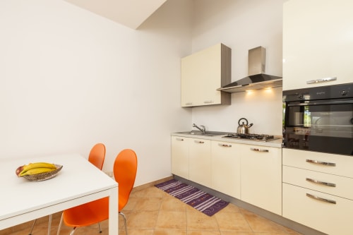Modern kitchen with cream cabinets, orange chairs, and gas cooktop in Agriturismo apartment, Bari Sardo