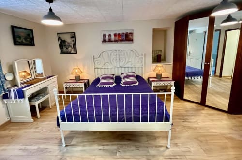 Chambre spacieuse du Gîte La Vieille Ferme avec lit en métal blanc, literie violette, lampes de chevet et parquet