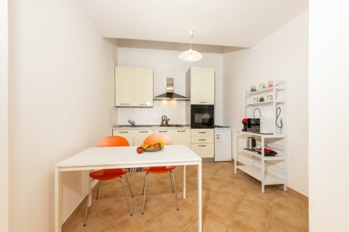Modern kitchen and dining area in Agriturismo Chiai Francesco apartment, Bari Sardo, with white cabinetry, orange chairs, and