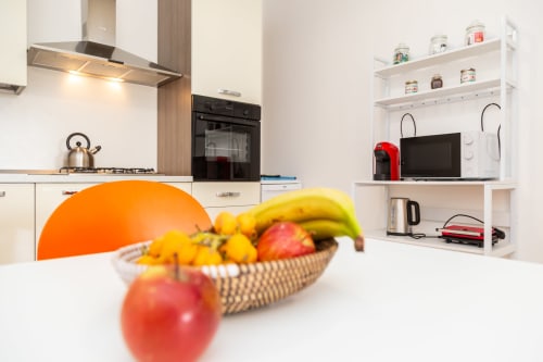 Modern kitchen apartment in Bari Sardo with fruit bowl, stainless steel appliances, and white shelving with microwave and