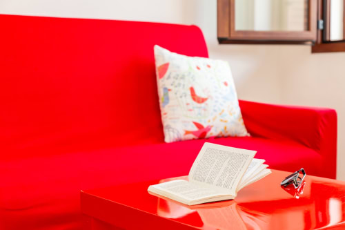 Bright red sofa with decorative pillow and open book on side table in Agriturismo apartment, Bari Sardo