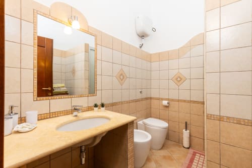 Spacious bathroom with beige tiles, curved countertop sink, toilet, and walk-in shower at Agriturismo Chiai Francesco in Bari