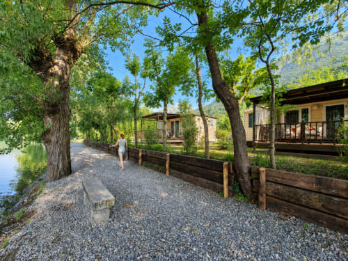 Sentiero in ghiaia fiancheggiato da alberi maestosi presso il resort Villaggio Lago Dorato a Carlazzo, Italia, con baite in legno e atmosfera tranquilla