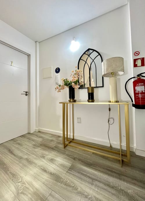 Modern hostel hallway at Casa Augusta with gold console table, black arch mirror, floral arrangement, and white door in
