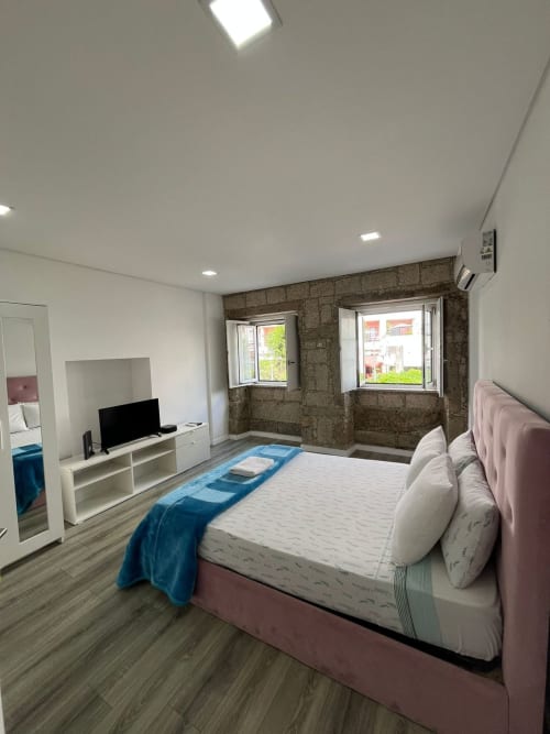 Modern private room at Casa Augusta hostel in Braga with pink bed, TV, wooden floors, and city views through windows