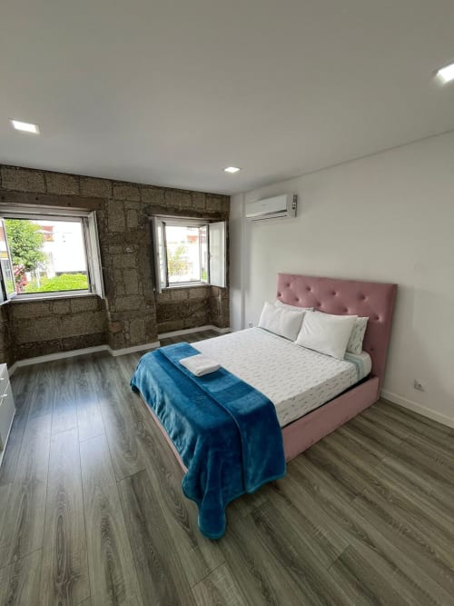 Modern bedroom at Casa Augusta hostel in Braga with pink bed, stone wall, wooden floors, and city view windows