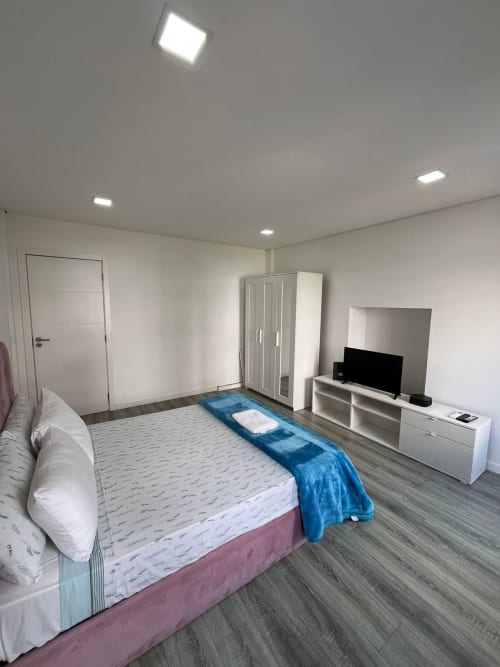 Modern private bedroom at Casa Augusta hostel with queen bed, TV, wardrobe, and wooden flooring in Braga, Portugal