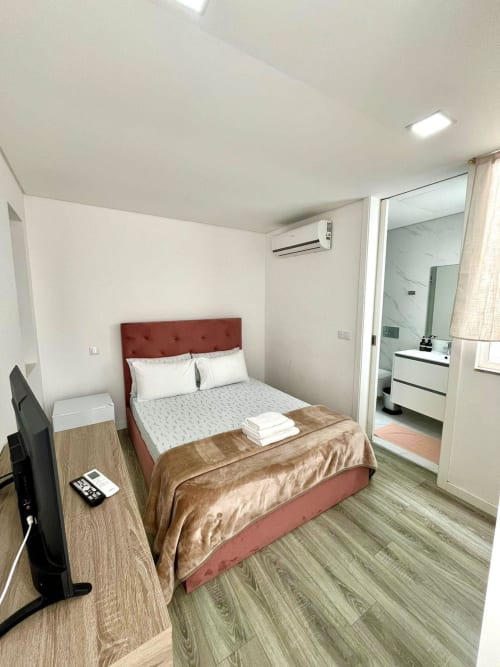 Modern bedroom at Casa Augusta hostel in Braga with terracotta bed frame, wood nightstand, flat-screen TV, and ensuite
