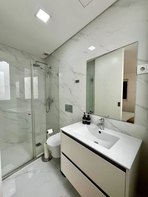 Modern bathroom at Casa Augusta hostel in Braga, Portugal with marble tiles, glass shower enclosure, and white vanity sink